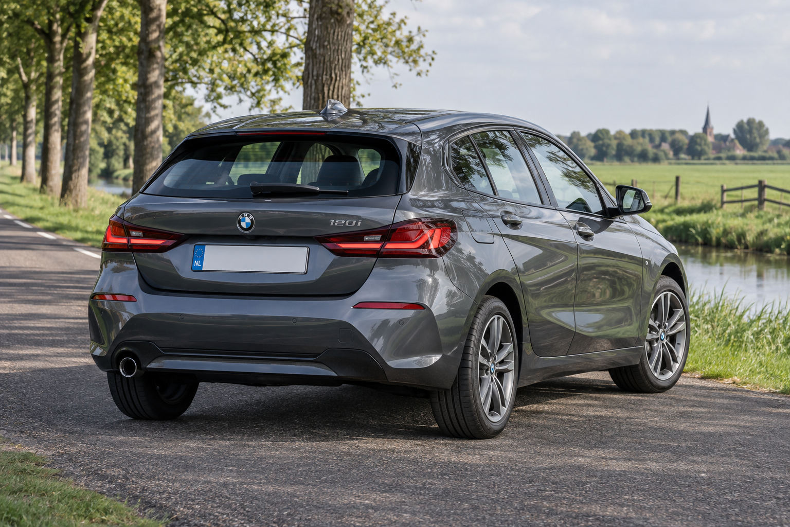 Grijze BMW 1 Serie F40 vijfdeurs, schuin van achteren aan een landelijke waterkant
