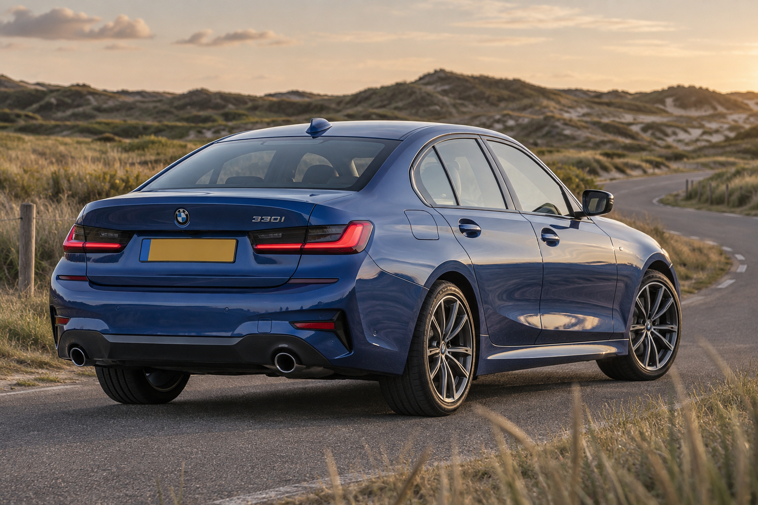 Blauwe BMW 330i Sedan langs een duinweg