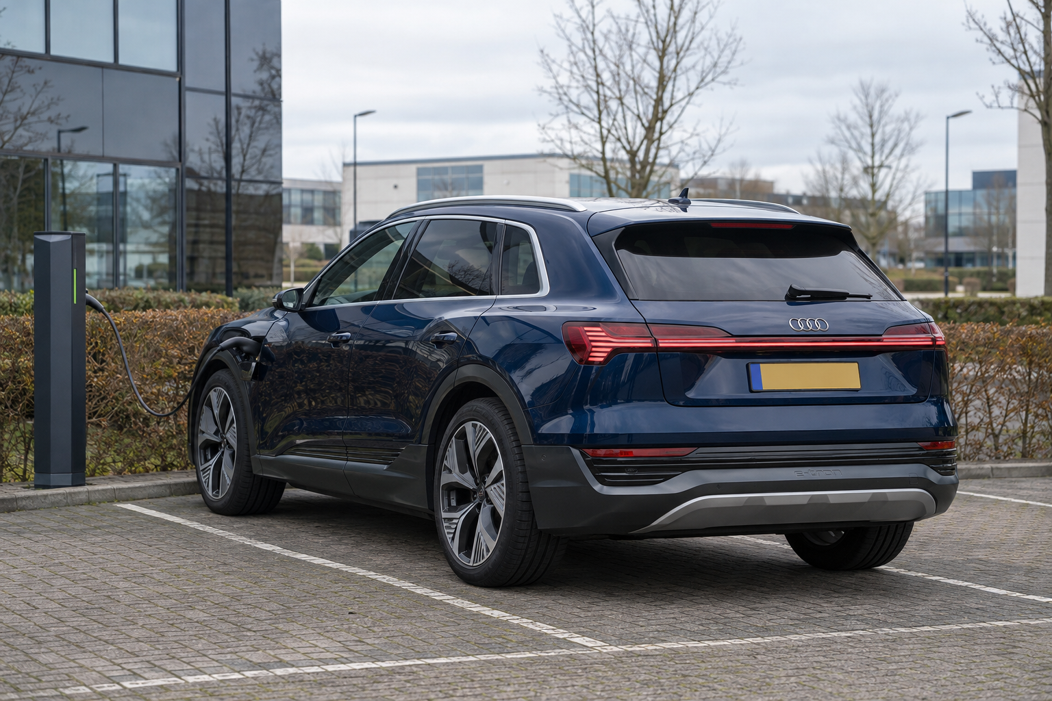 Blauwe Audi Q8 e-tron SUV aan een laadpaal bij een kantoorgebouw