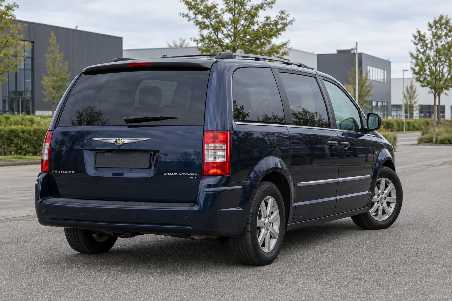 Donkerblauwe Chrysler Grand Voyager van achteren op een rustig bedrijventerrein