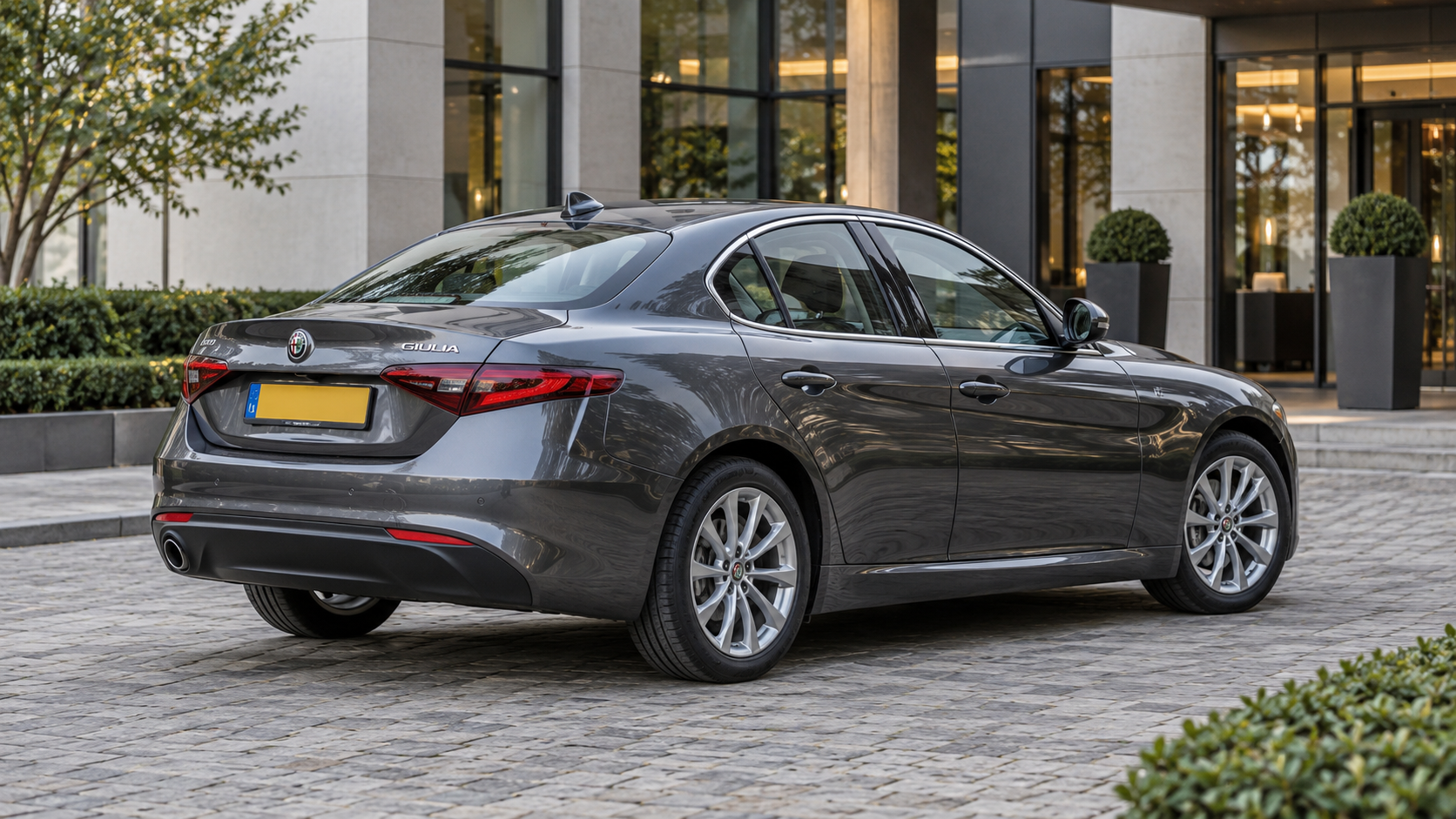 Grijze Alfa Romeo Giulia sedan van schuin achteren voor een bedrijfspand