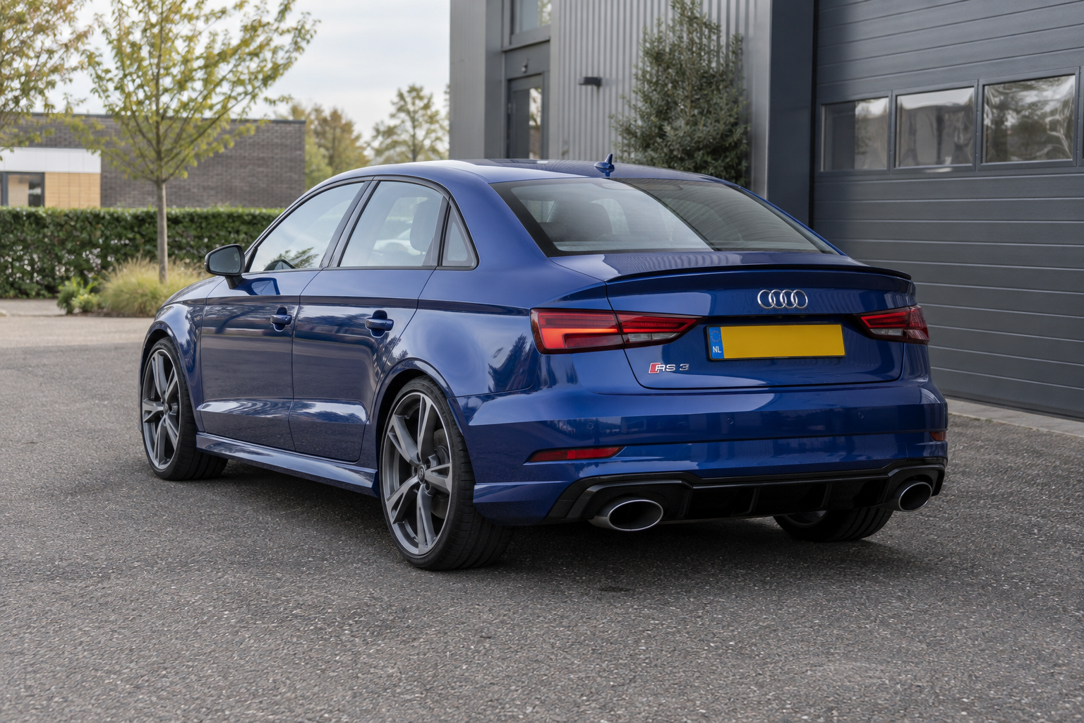 Blauwe Audi RS 3 Limousine als modelillustratie, van achteren gezien bij een bedrijfspand