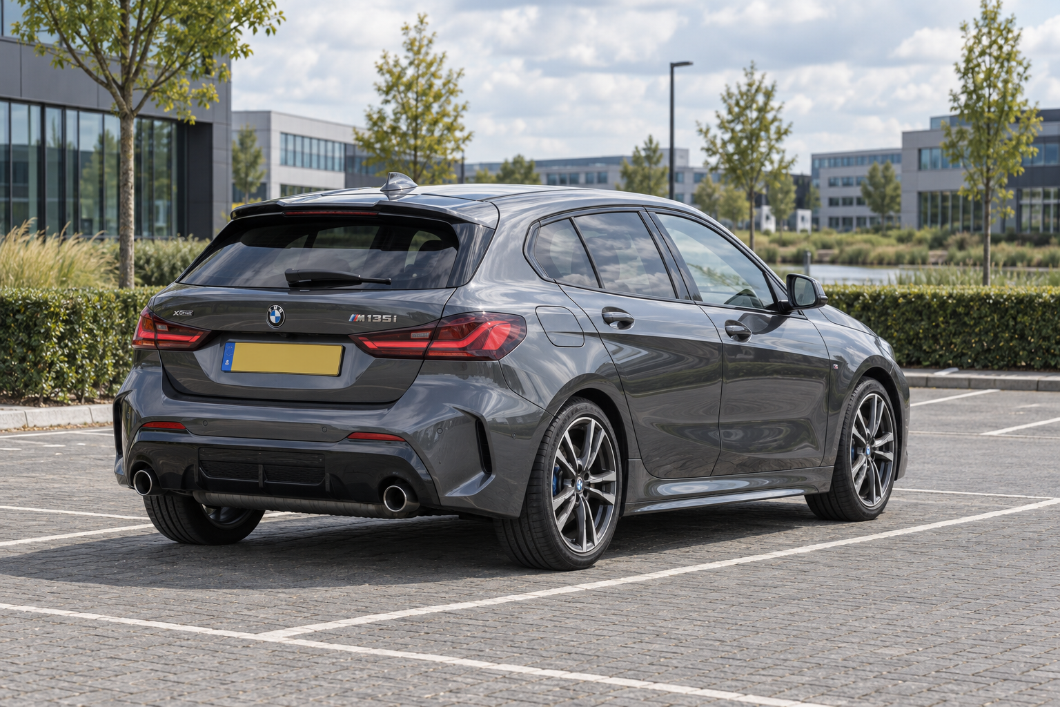 Grijze BMW 1 Serie F40 in sportieve uitvoering, gezien van achteren bij een kantoorgebouw